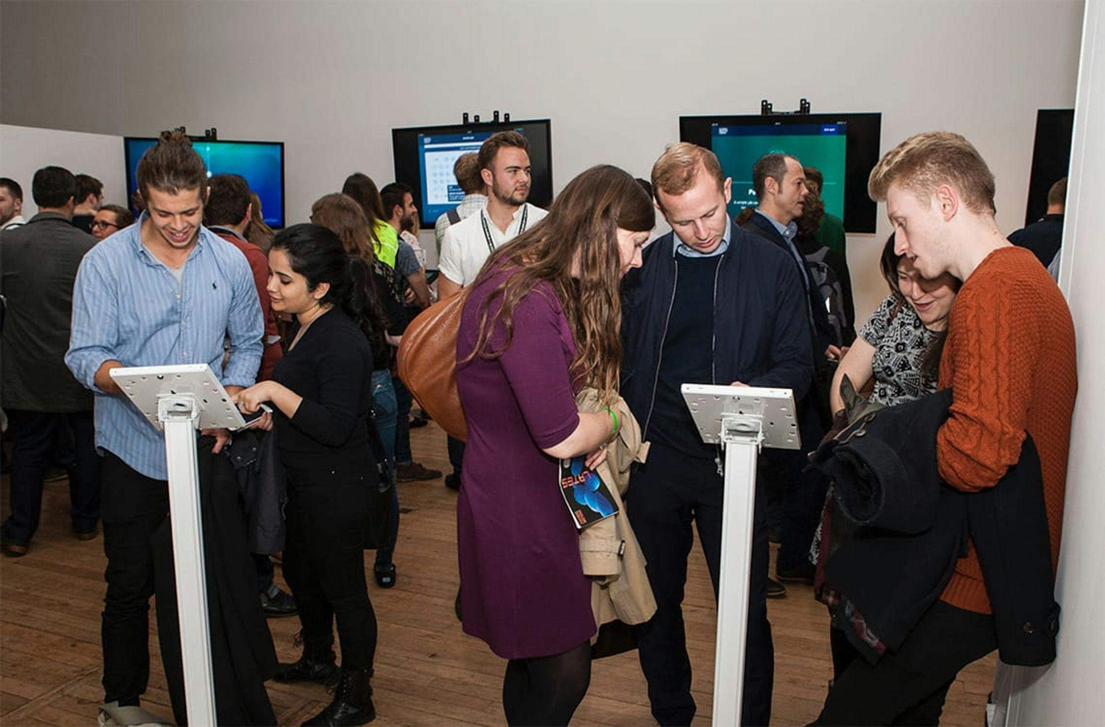 A photo taken at the Global Health Check physical installation. Various screens show the final visualizations as people look and interact with each one around the room.