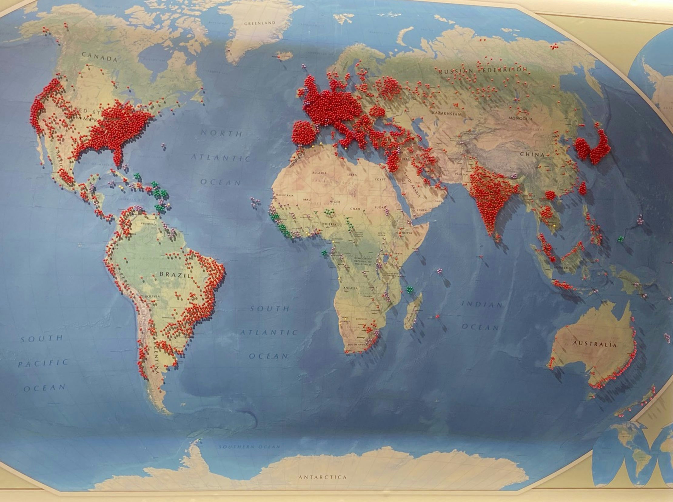 A paper world map covered in red pins where COVID cases have occurred. 