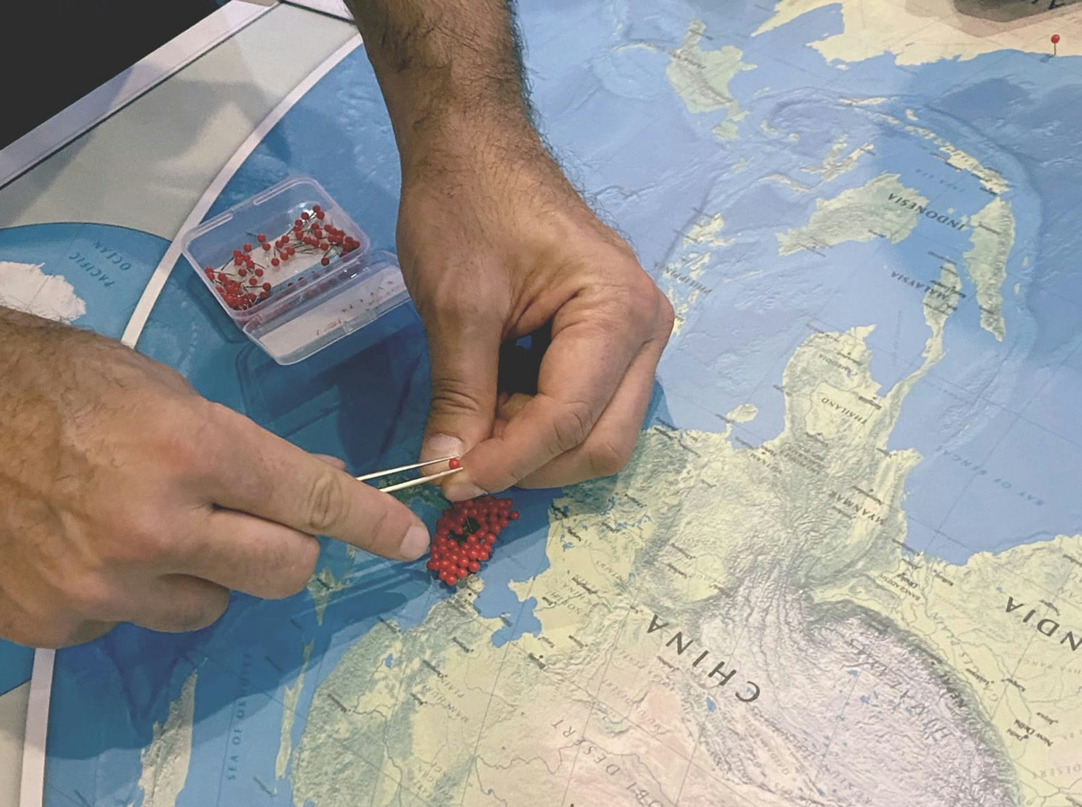 A close up of a paper map and a pair of hands, carefully pinning red dots in a dense cluster on the map.